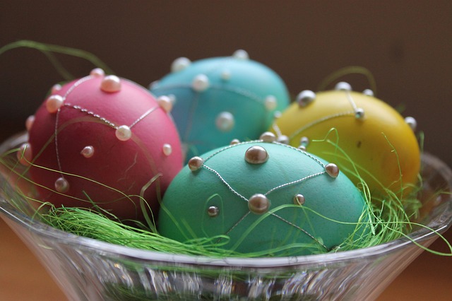Four pretty and colorful Easter Eggs sit in a glass bowl with fake green straw.